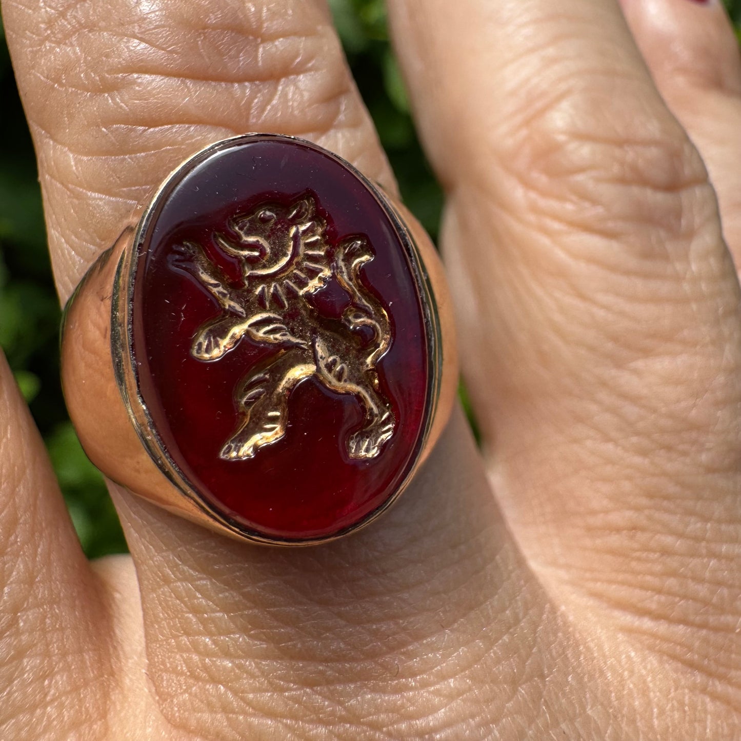 טבעת חותם זהב צהוב 14 קראט משובצת אבן אדומה חלקה ודמות אריה מוזהבת בעיצוב עתיק.
