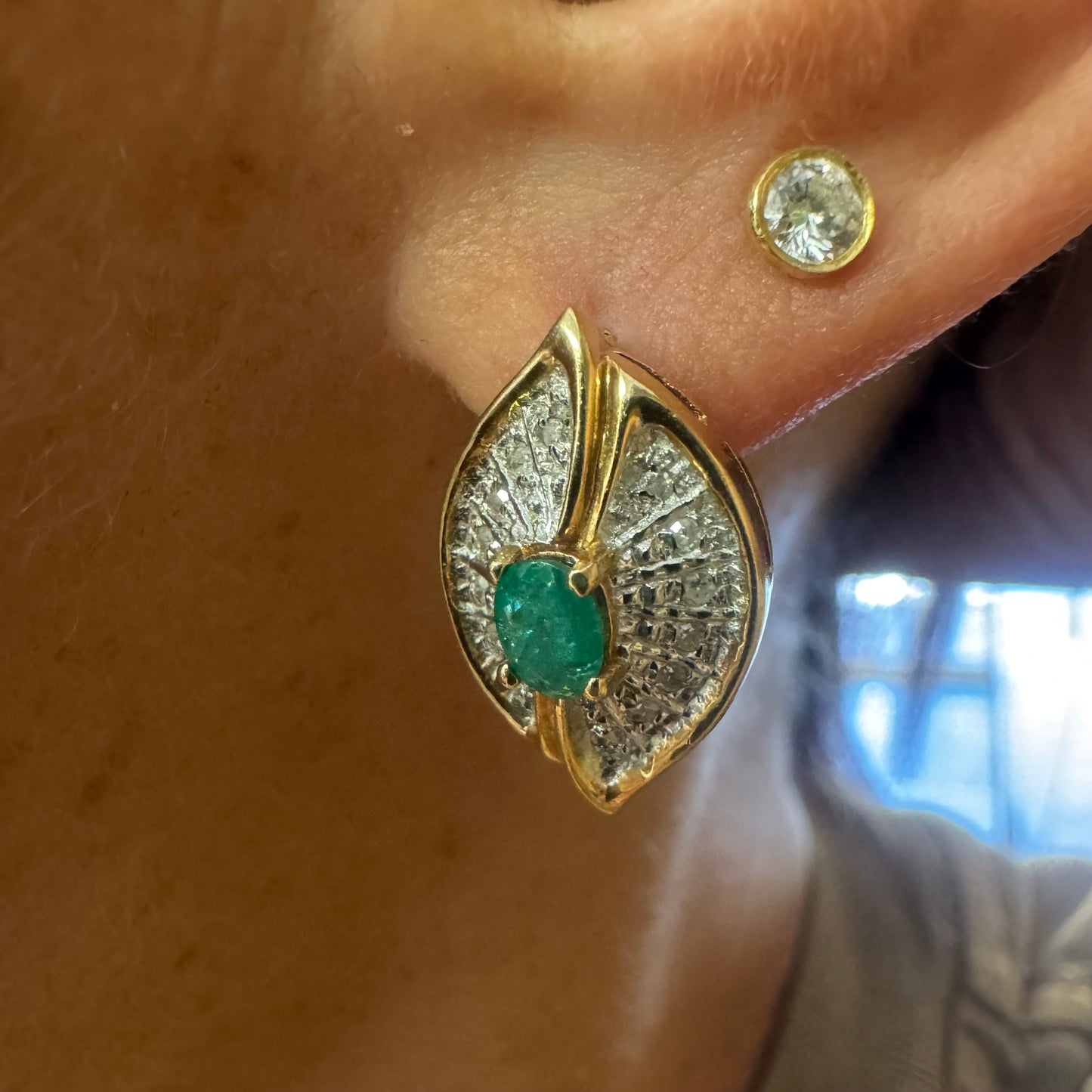 עגילים צמודים לאוזן, זהב צהוב 14 קראט, משובצים אמרלד במרכז, וסביבן פיתוחים משובצים יהלומים, שמעניקים מראה של ניצוץ רך ואלגנטי
