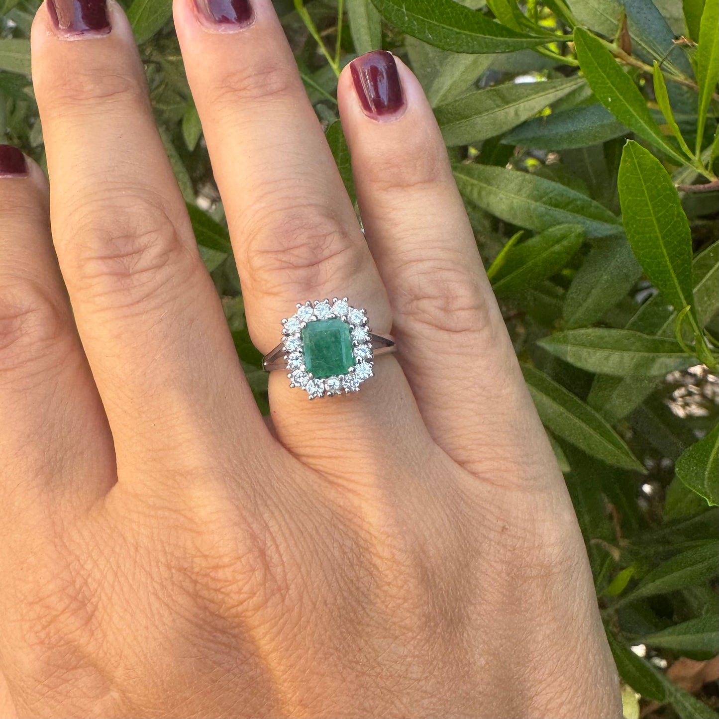 18K gold ring set with a green Emerald at the center, surrounded by a halo of sparkling round Diamonds.