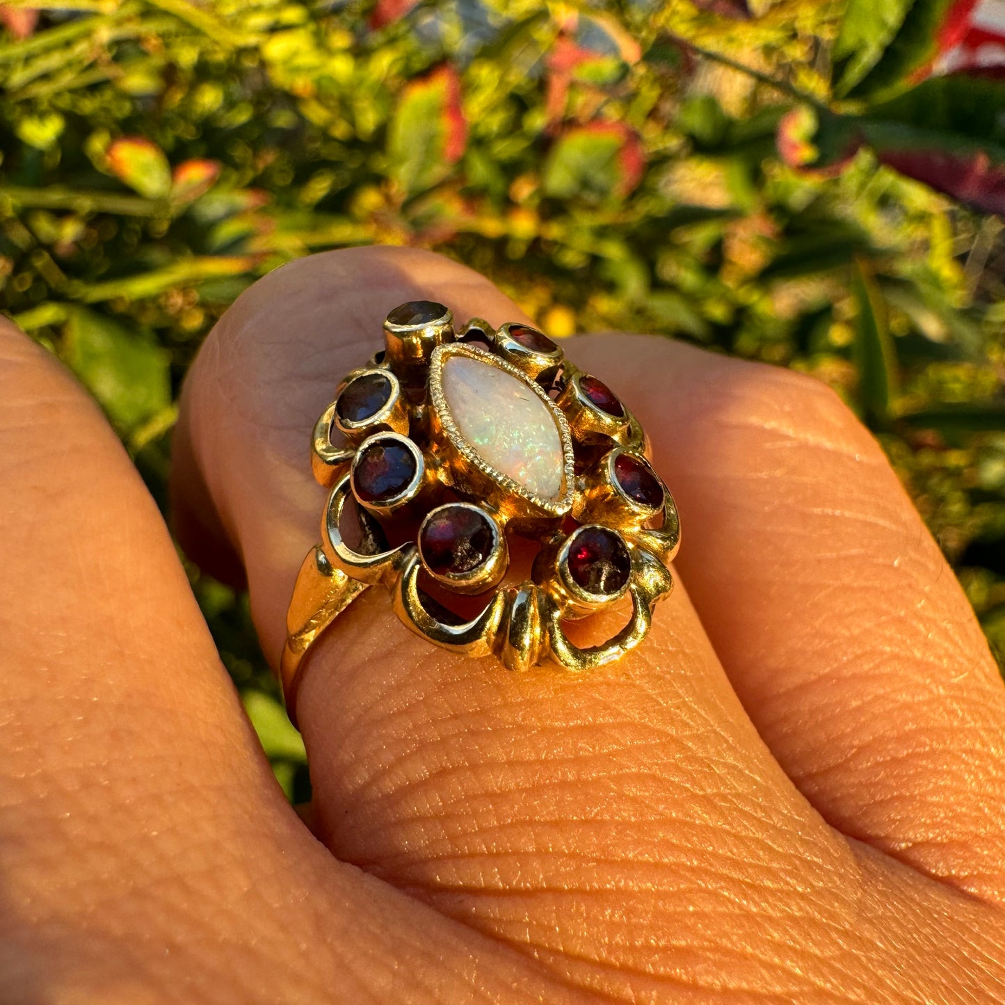 14K gold ring set with a luminous marquise-cut Opal at the center, surrounded by deep red Garnet cabochons
