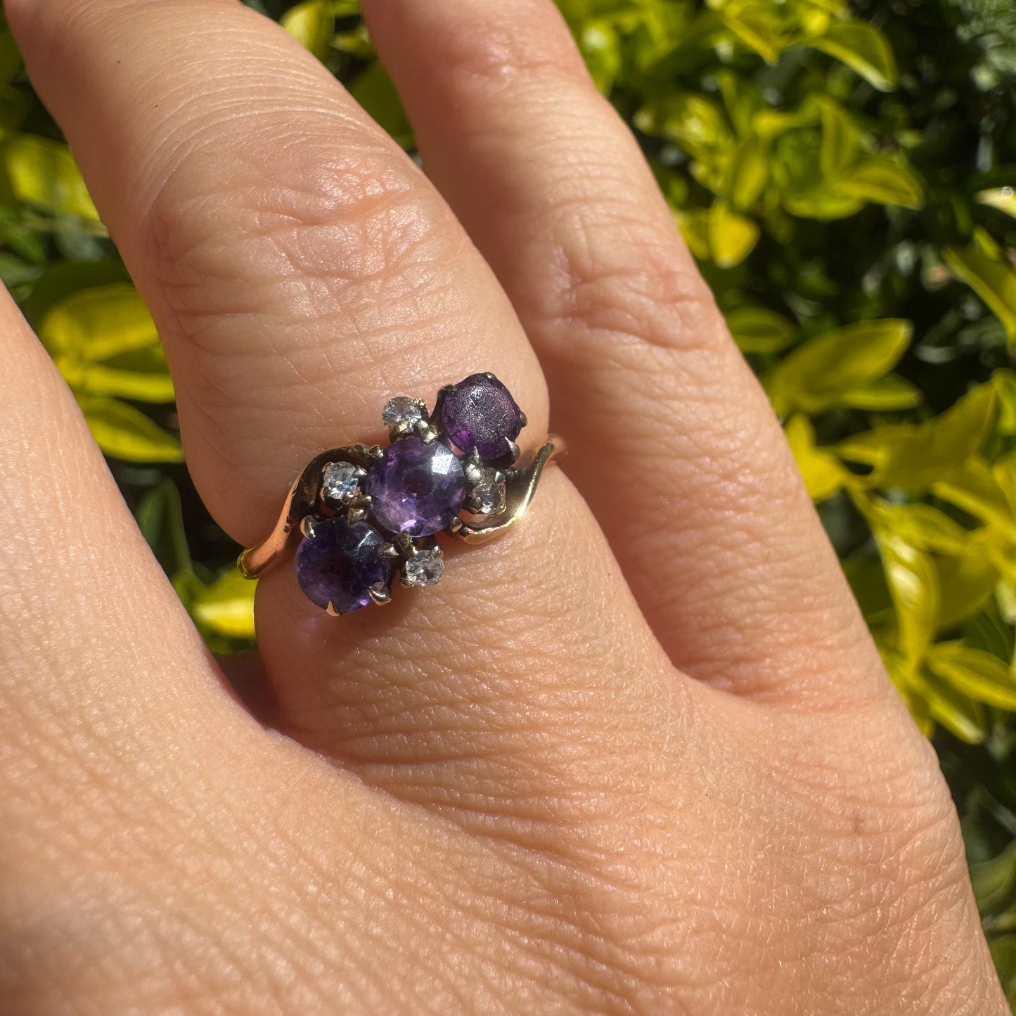 14K gold ring set with three round purple amethysts, accented by small sparkling Diamonds.
