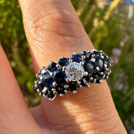 18K gold ring set with a brilliant-cut central Diamond, surrounded by a striking cluster of deep blue Sapphires.