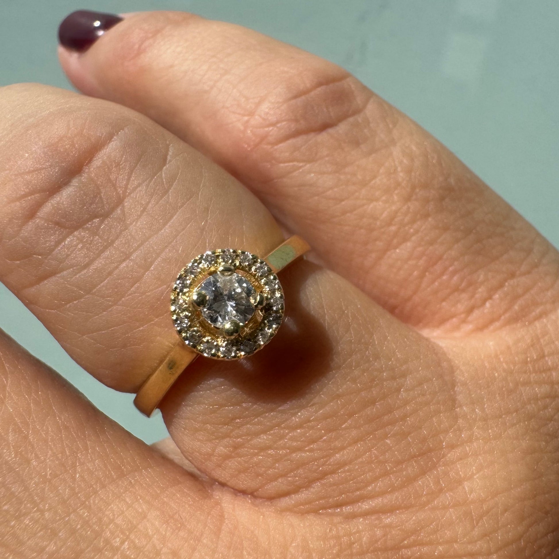 טבעת זהב צהוב 14 קראט משובצת יהלום מרכזי עגול, המוקף בהילה (Halo) של יהלומים מנצנצים.