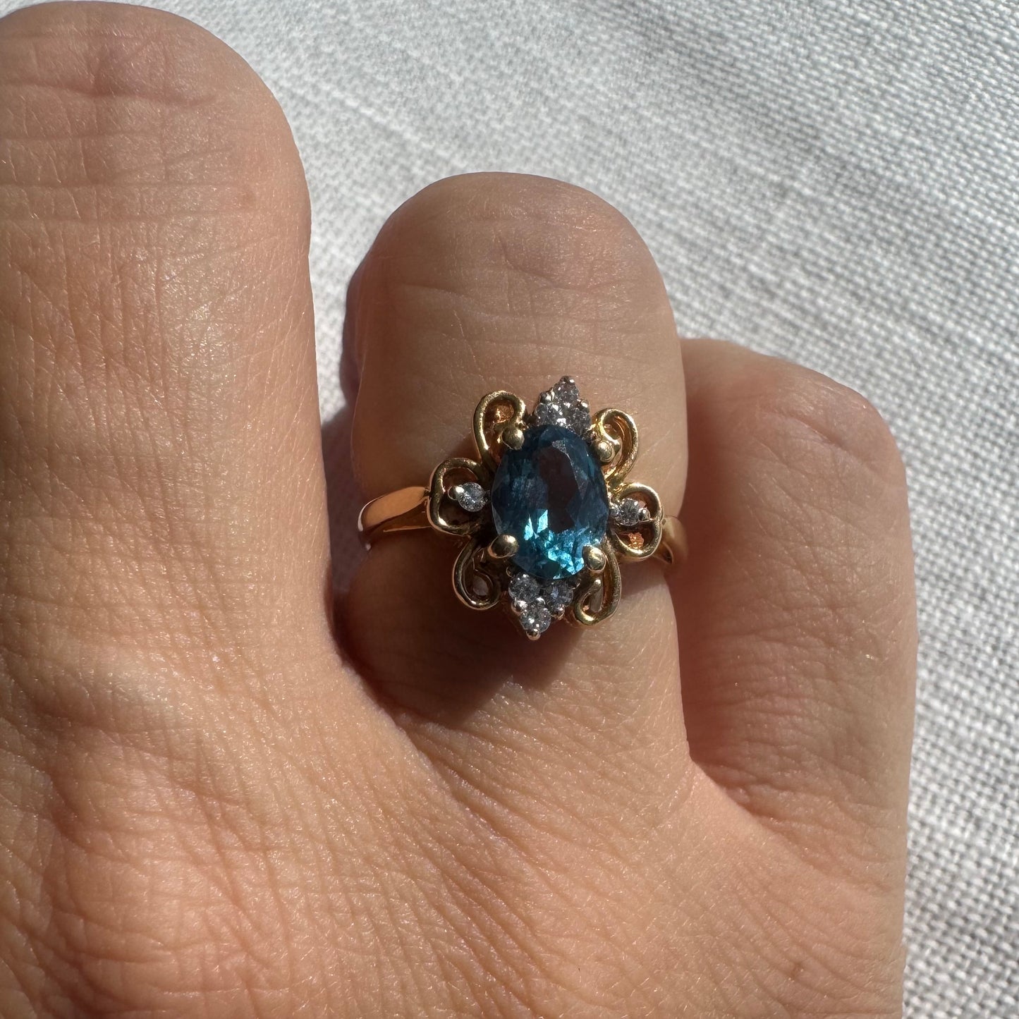18K gold ring featuring an oval-cut Blue Topaz at the center, accented by sparkling side Diamonds and elegant scroll details.
