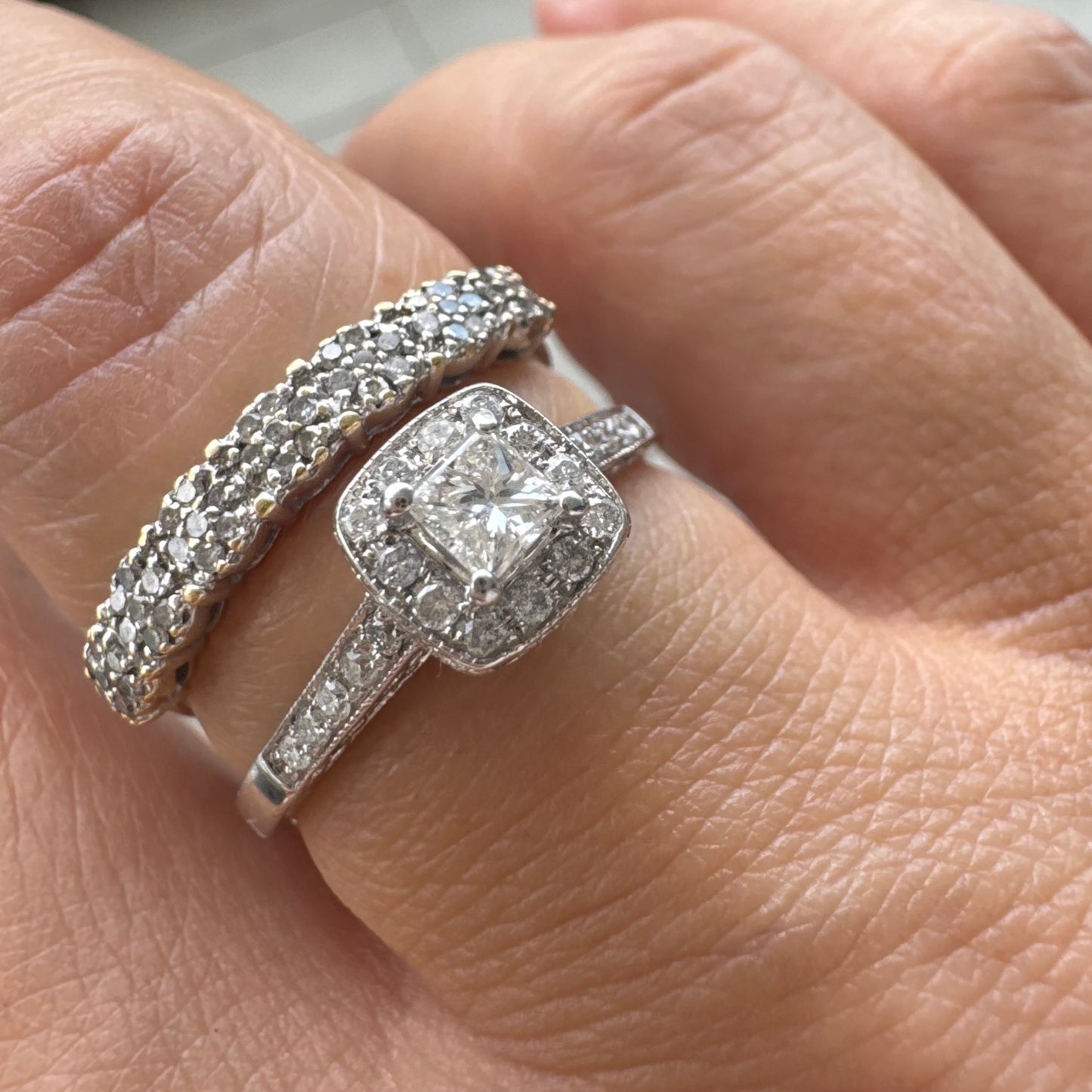 טבעת זהב לבן 14 קראט משובצת יהלום מרכזי בחיתוך פרינסס, מוקף הילת יהלומים קטנים וזרוע משובצת פאווה