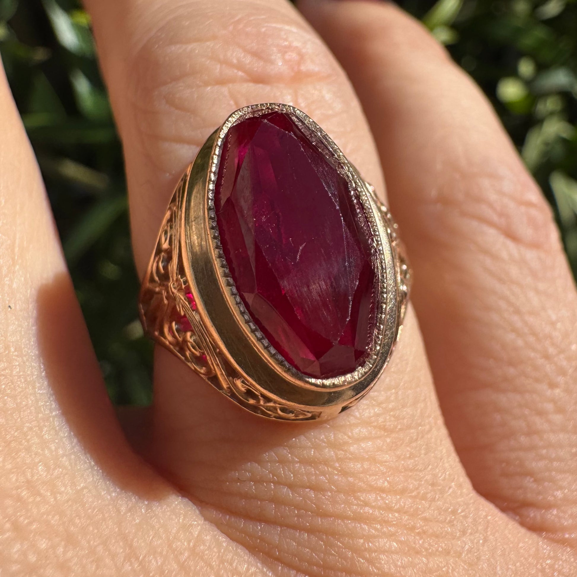 טבעת זהב צהוב 14 קראט משובצת אבן רובי אובלית בצבע אדום עמוק, במסגרת מעוטרת ובעבודת פיליגרן עדינה על הכתפיים.
