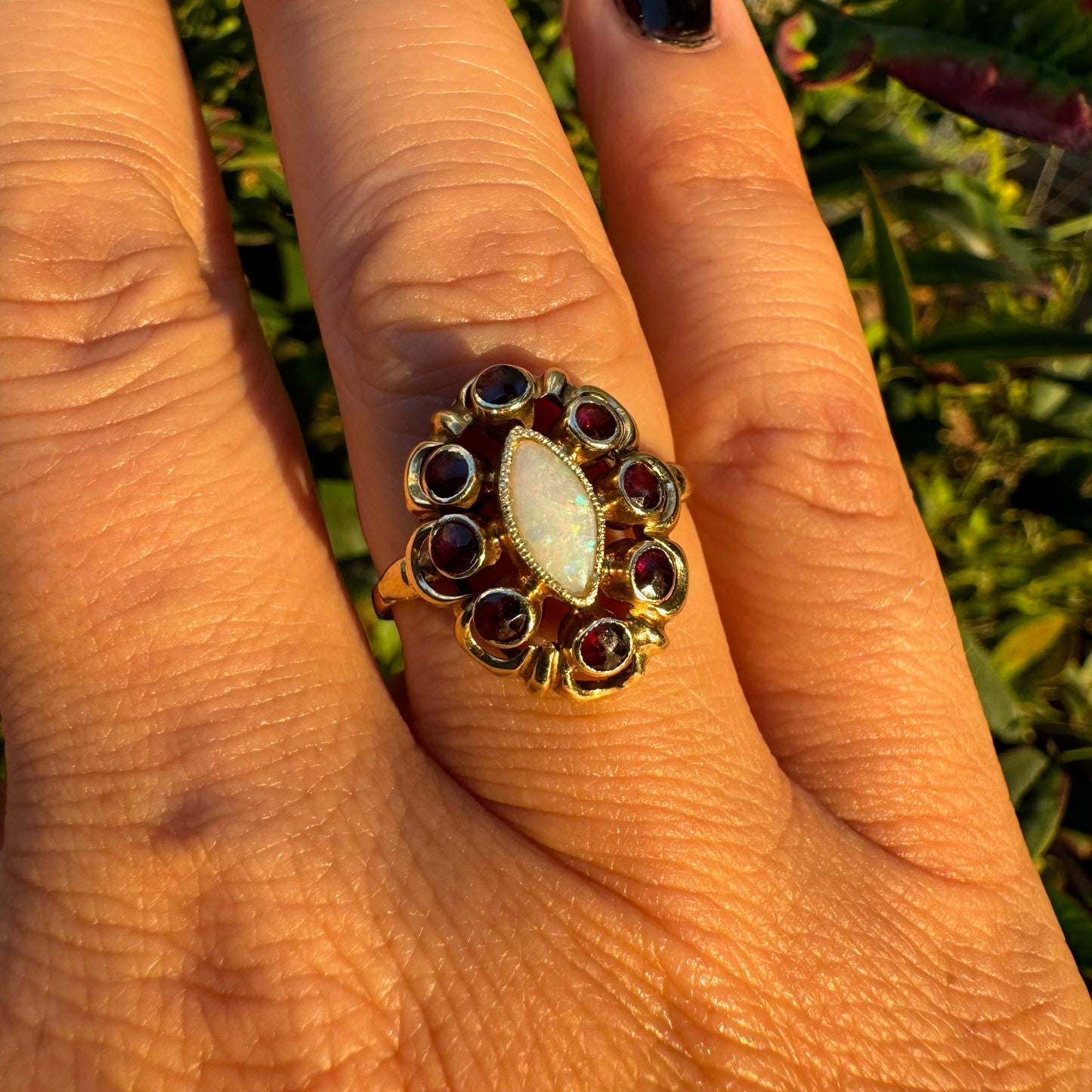 14K gold ring set with a luminous marquise-cut Opal at the center, surrounded by deep red Garnet cabochons