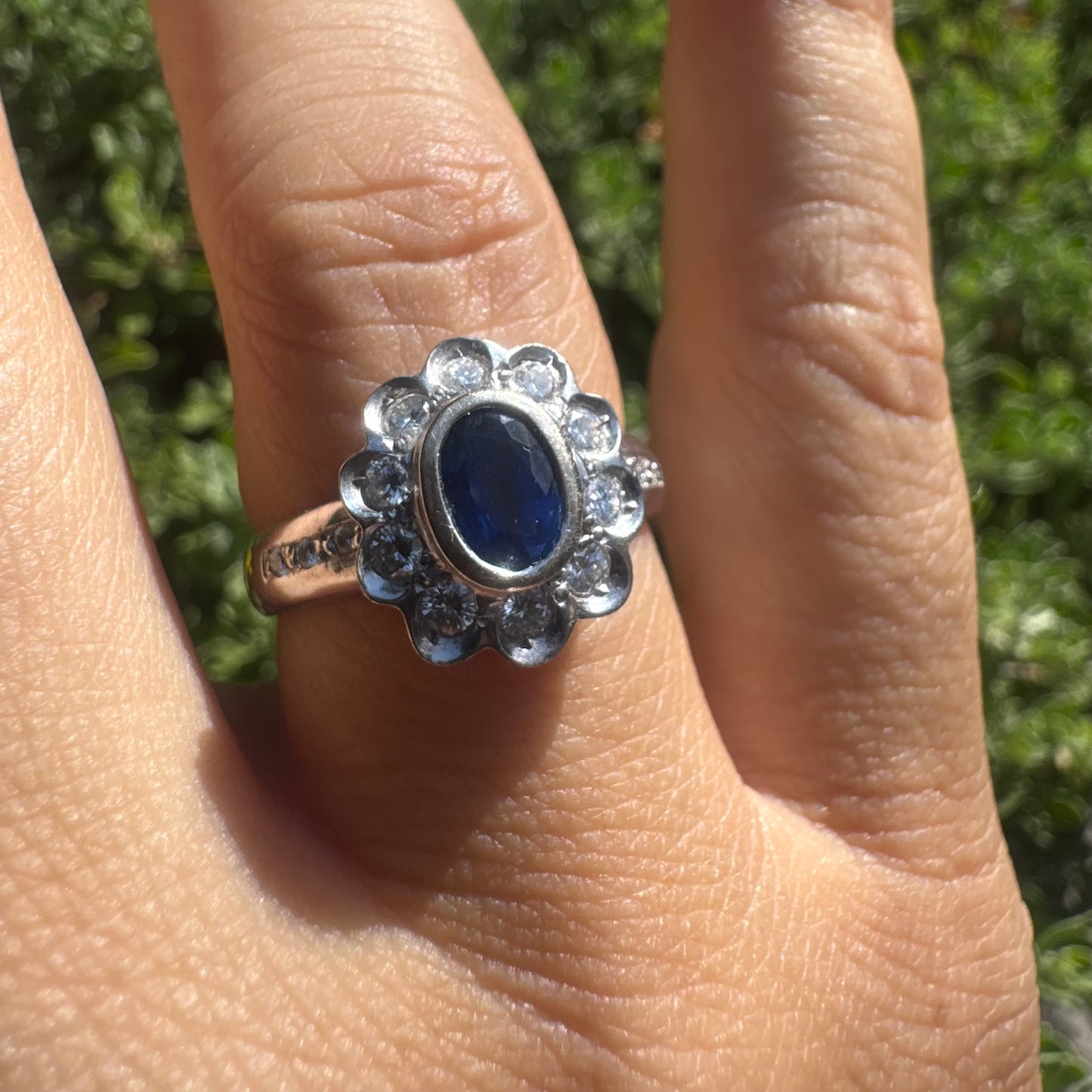 18K gold ring set with an oval blue Sapphire surrounded by a halo of round Diamonds in a flower-shaped design.