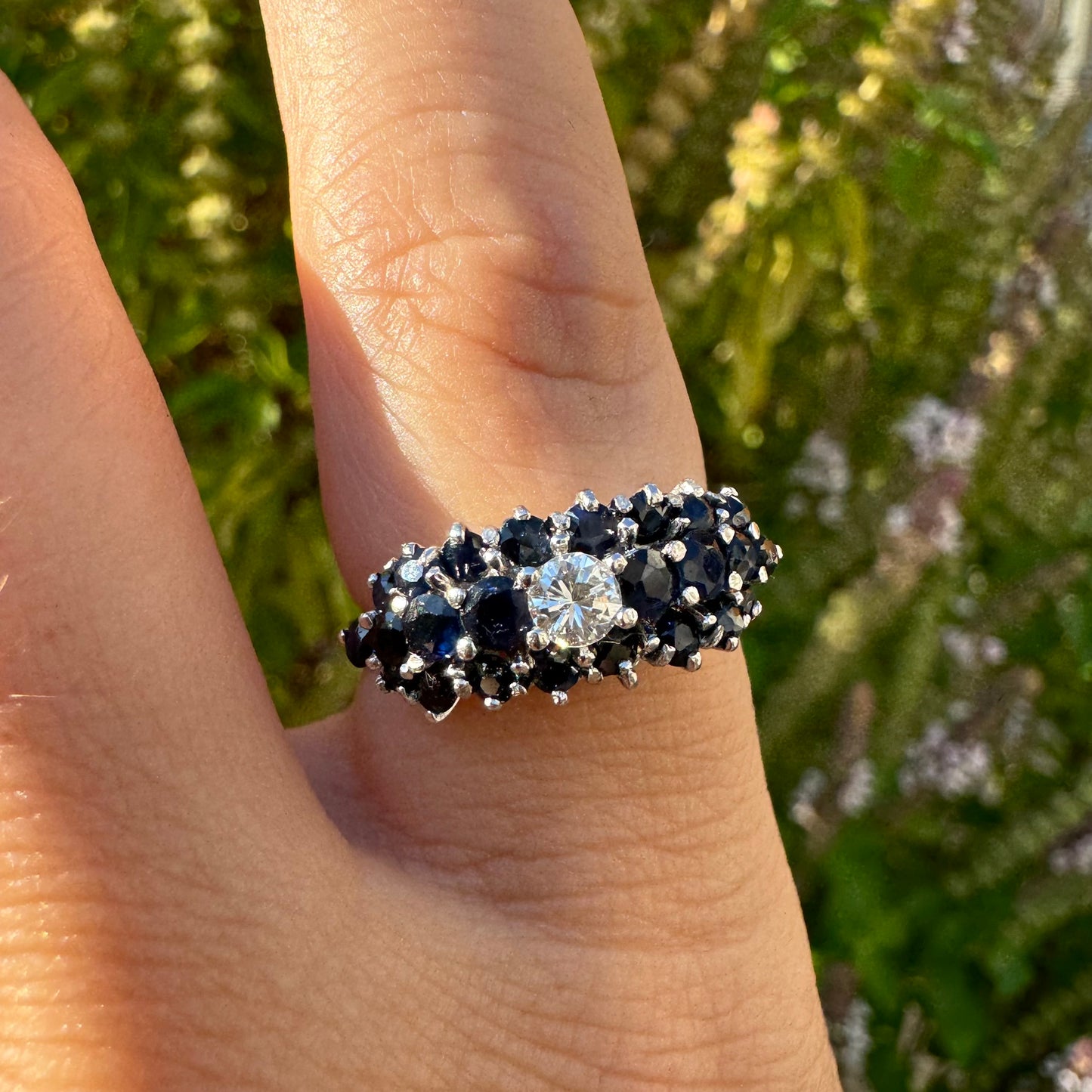 18K gold ring set with a brilliant-cut central Diamond, surrounded by a striking cluster of deep blue Sapphires.