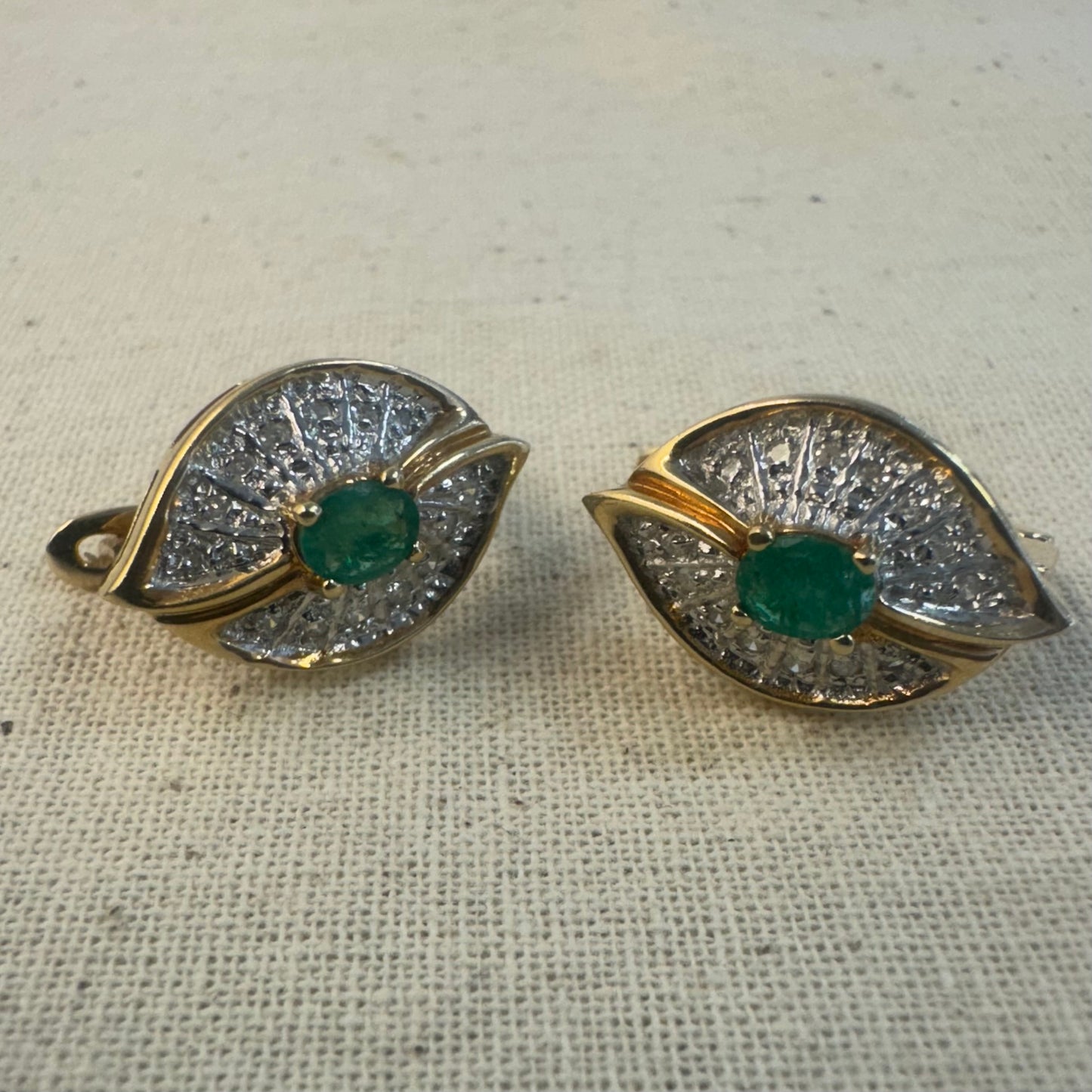 עגילים צמודים לאוזן, זהב צהוב 14 קראט, משובצים אמרלד במרכז, וסביבן פיתוחים משובצים יהלומים, שמעניקים מראה של ניצוץ רך ואלגנטי