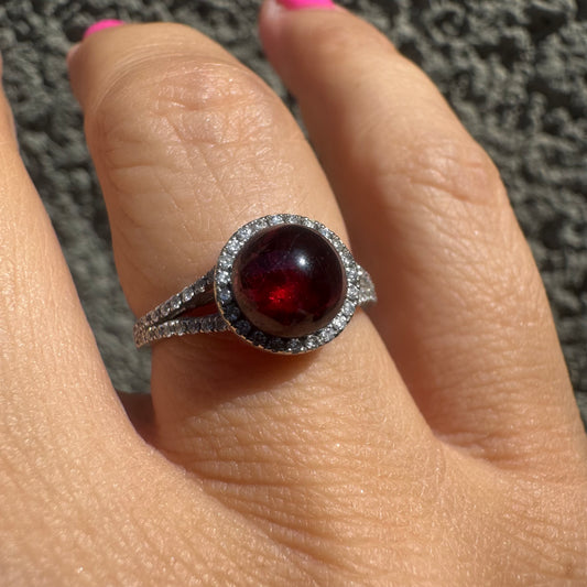 טבעת זהב לבן 14 קראט משובצת אבן גרנט בחיתוך קבושון, מוקפת יהלומים נוצצים. 
