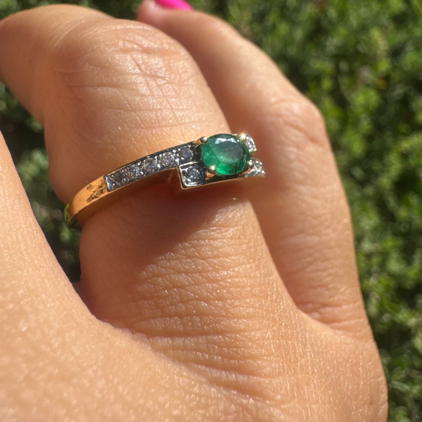18K gold ring set with an oval green Emerald at the center, accented with sparkling Diamonds along the band.