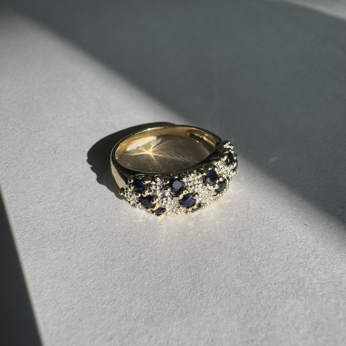 טבעת זהב צהוב 10 קראט משובצת אבני ספיר כהות ויהלומים בעיצוב קלאסי ורומנטי.