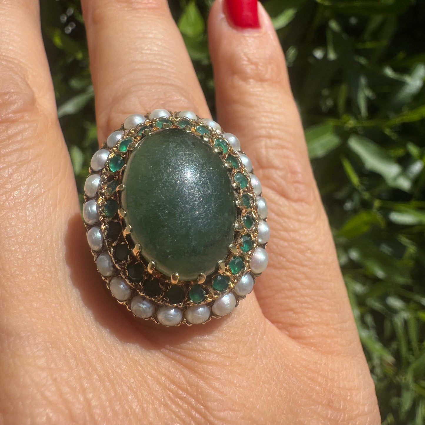 14K gold set with a large oval green Jade at its center, surrounded by concentric halos of sparkling Emeralds and delicate pearls