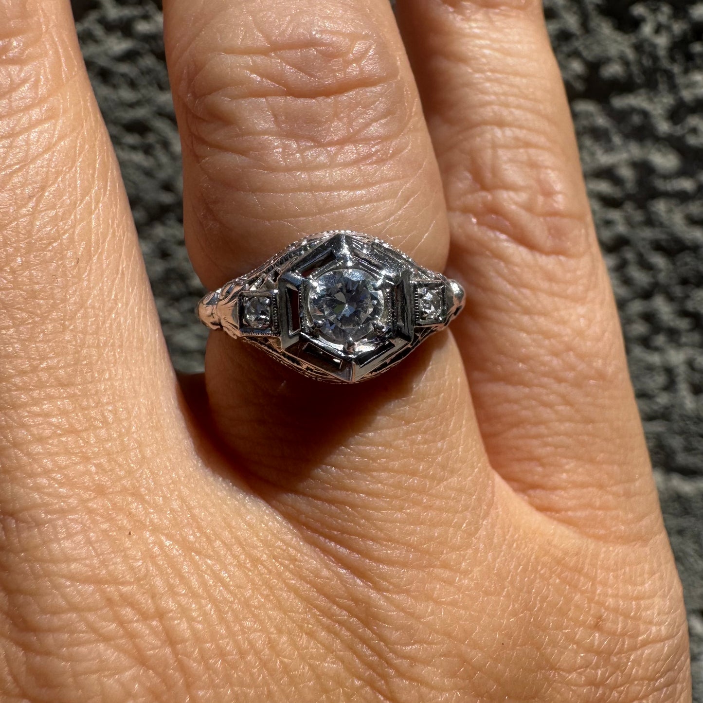 14K gold ring set with a central round diamond, framed by geometric Art Deco details and additional accent stones.