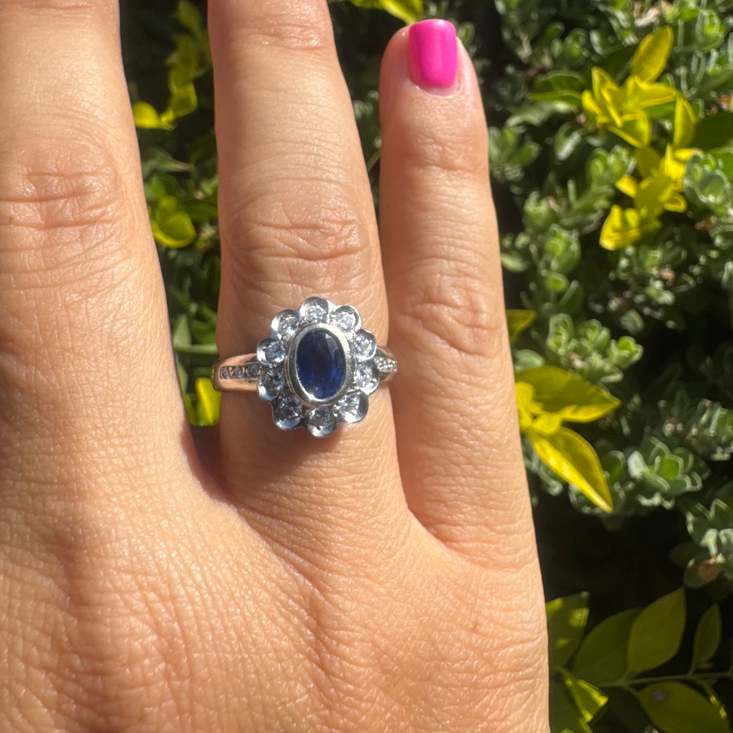 18K gold ring set with an oval blue Sapphire surrounded by a halo of round Diamonds in a flower-shaped design.