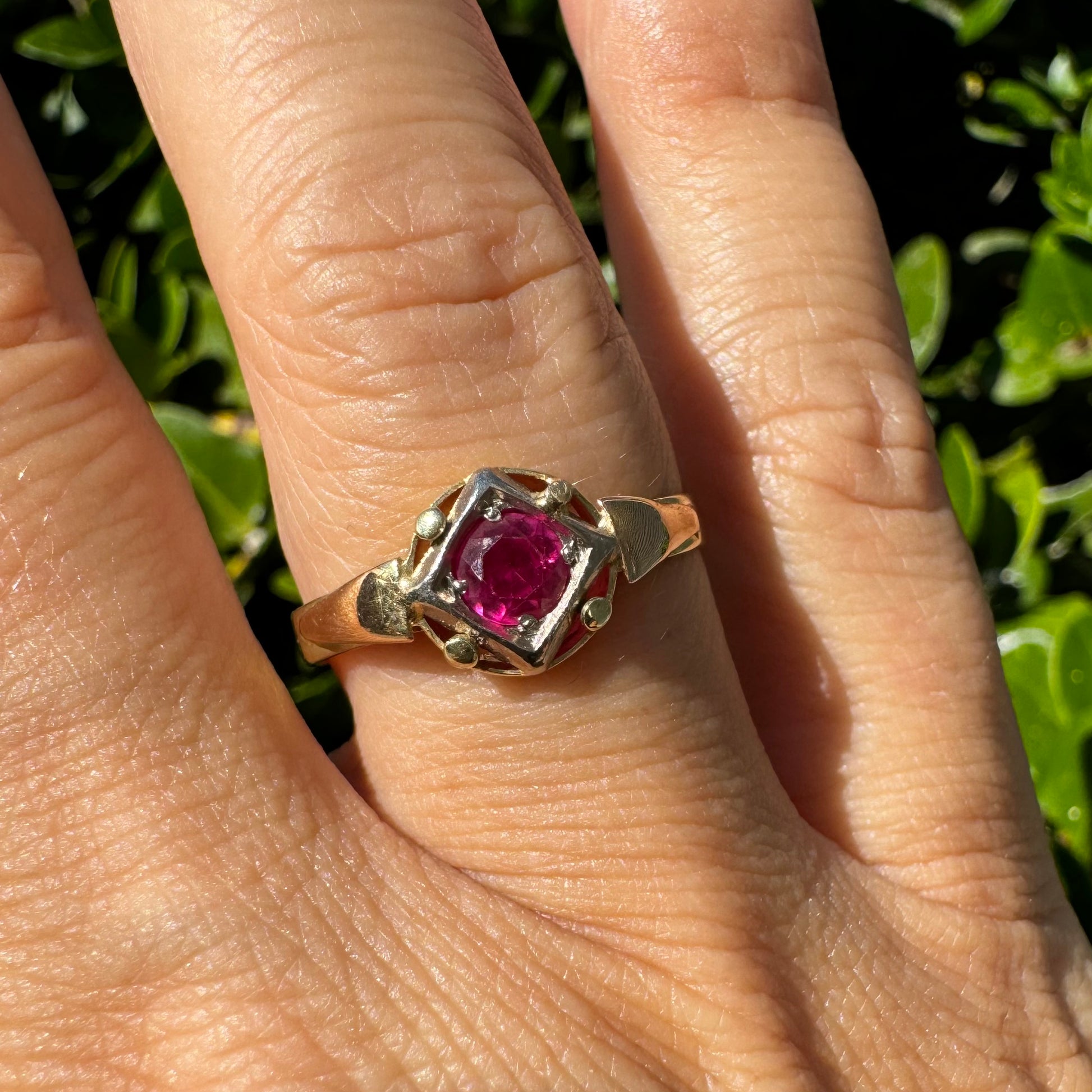 טבעת זהב צהוב 14 קראט משובצת אבן רובי עגול ובוהק בתוך מסגרת זהב גאומטרית.