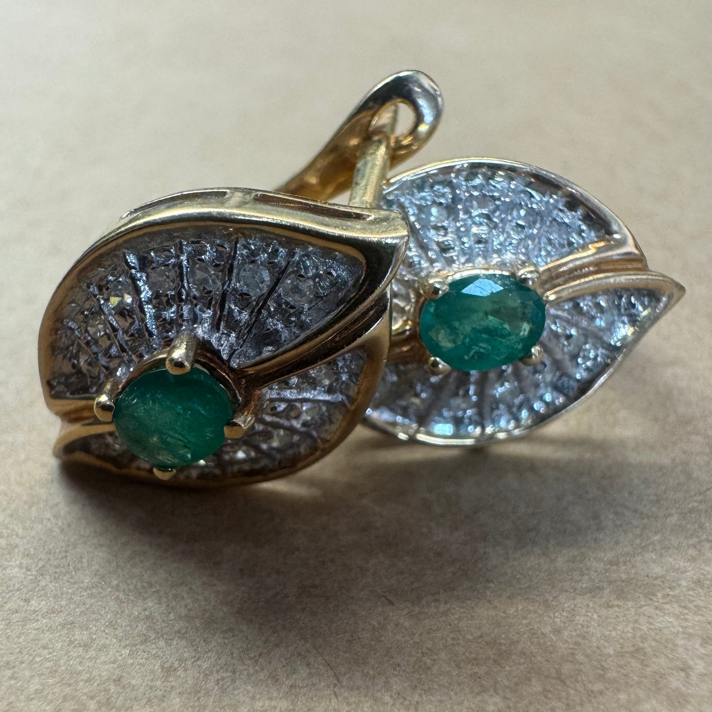 עגילים צמודים לאוזן, זהב צהוב 14 קראט, משובצים אמרלד במרכז, וסביבן פיתוחים משובצים יהלומים, שמעניקים מראה של ניצוץ רך ואלגנטי