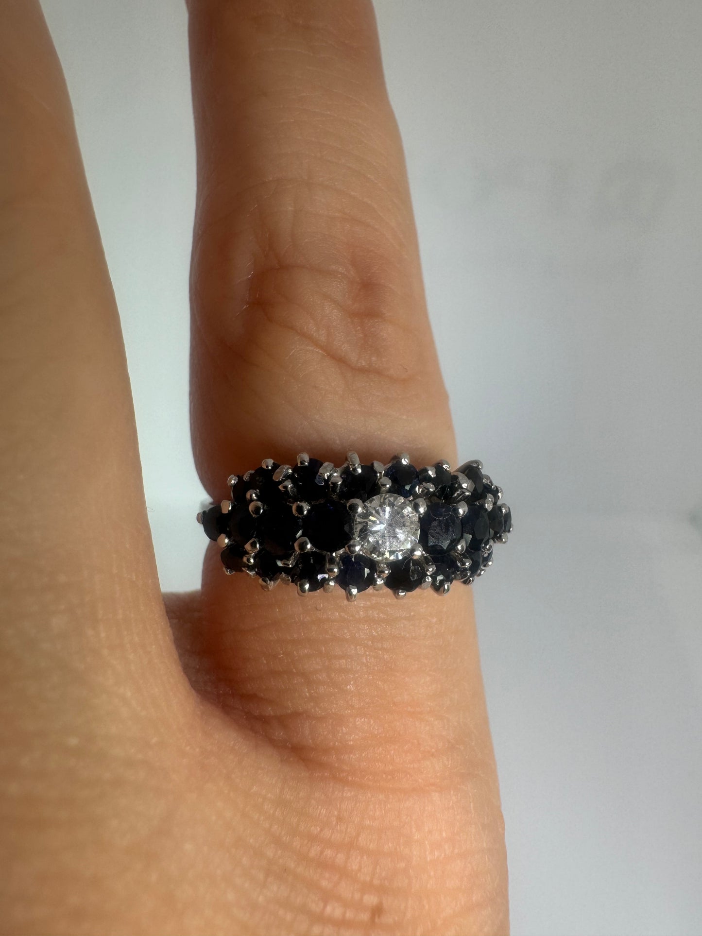 18K gold ring set with a brilliant-cut central Diamond, surrounded by a striking cluster of deep blue Sapphires.