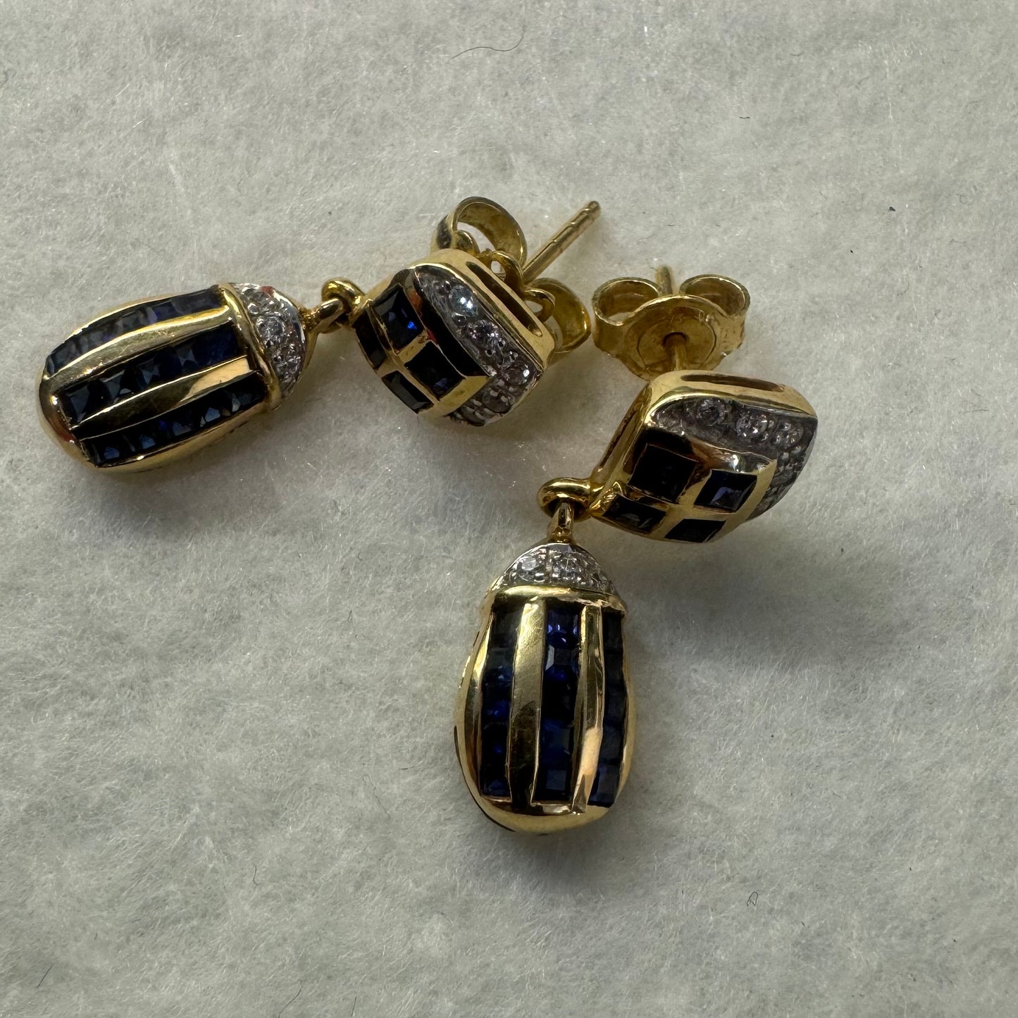 עגילי זהב צהוב 18 קראט תלויים, משובצים אבני ספיר כחולות בגוון כחול עמוק בעיצוב גיאומטרי, בשילוב יהלומים מנצנצים
