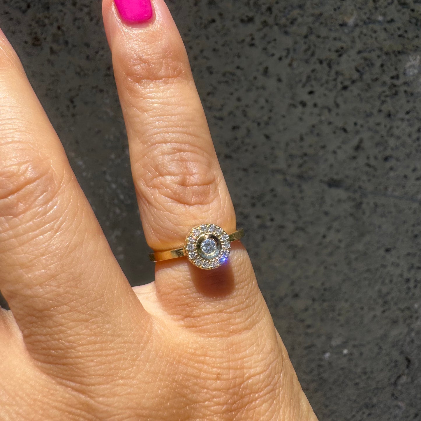 14K gold ring set with a bezel-set central Diamond, surrounded by a sparkling halo of brilliant-cut Diamonds.