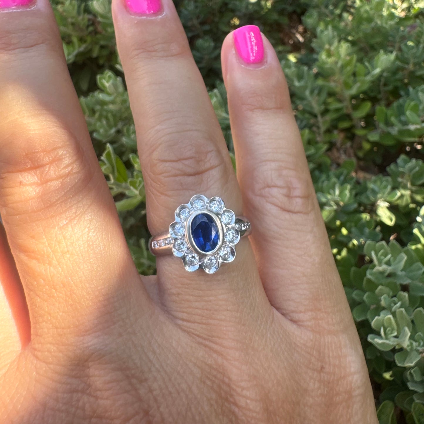 18K gold ring set with an oval blue Sapphire surrounded by a halo of round Diamonds in a flower-shaped design.