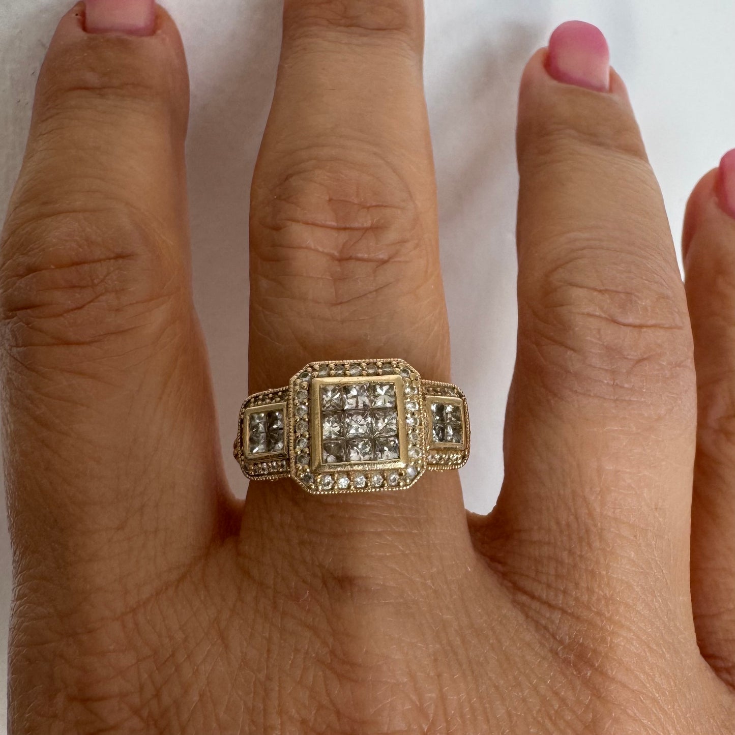 טבעת זהב צהוב 14 קראט משובצת יהלומים בחיתוך פרינסס במרכז, מוקפת הילה של יהלומים צדדיים.