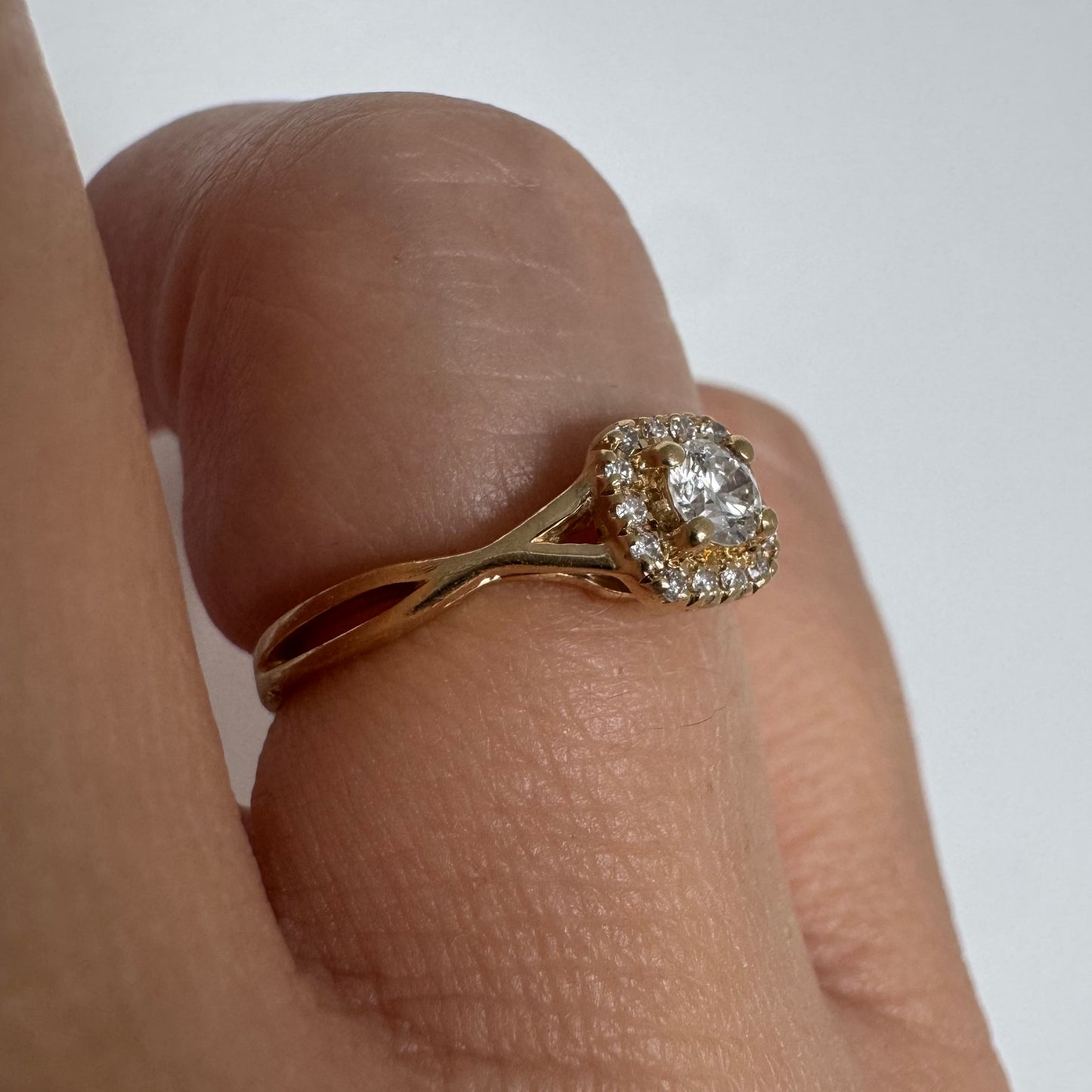 טבעת זהב 14 קראט משובצת יהלום מרכזי עגול ומבריק, מוקף הילה עדינה של יהלומים המעצימים את הברק