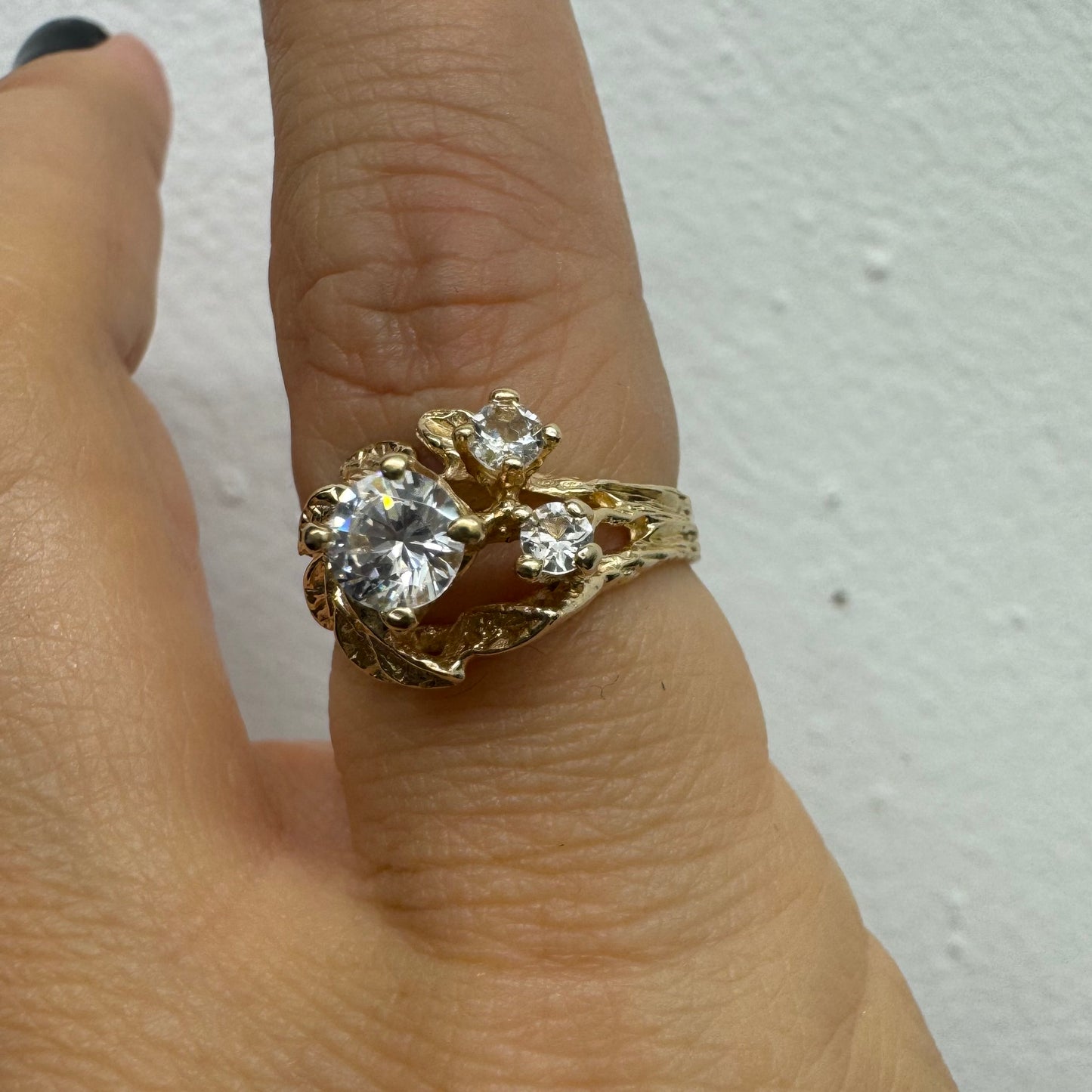 טבעת זהב צהוב 14 קראט בעלת עיצוב אורגני עשיר עם עלים מגולפים סביב שלוש אבנים שקופות נוצצות. (לא יהלומים)