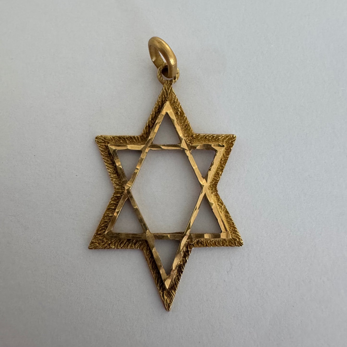 תליון מגן דוד מזהב צהוב 14 קראט בעיצוב פתוח, עם טקסטורה עדינה בשוליים המוסיפה עומק ואופי.