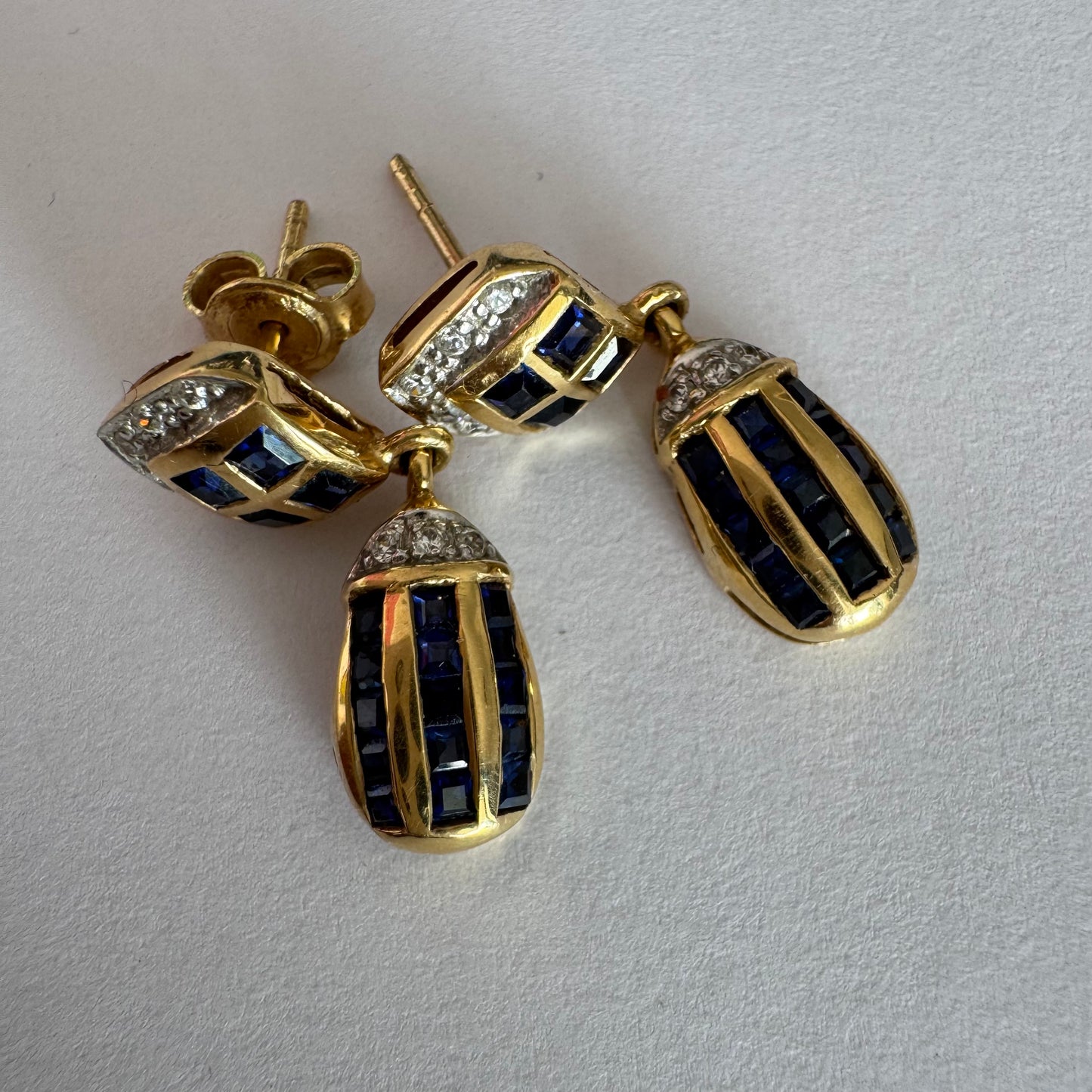 עגילי זהב צהוב 18 קראט תלויים, משובצים אבני ספיר כחולות בגוון כחול עמוק בעיצוב גיאומטרי, בשילוב יהלומים מנצנצים