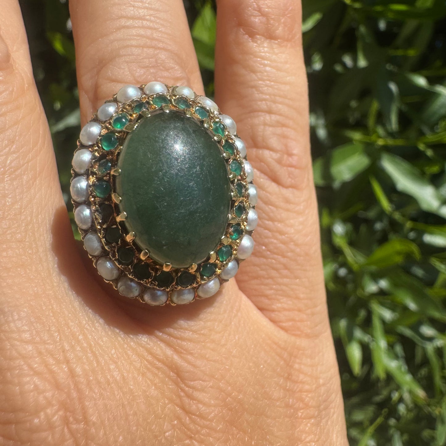 14K gold set with a large oval green Jade at its center, surrounded by concentric halos of sparkling Emeralds and delicate pearls