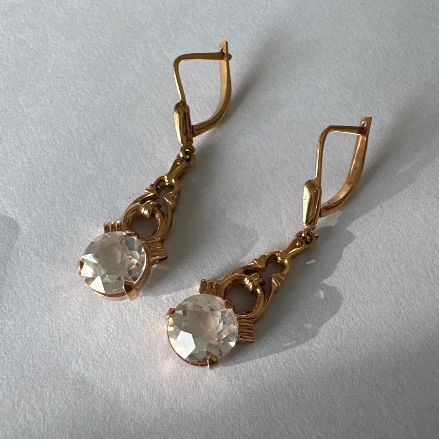 עגילי זהב 14 קראט, תלויים, בעיצוב עדין ונוסטלגי, משובצים באבני חן חתוכות שקופות בסגנון עתיק.