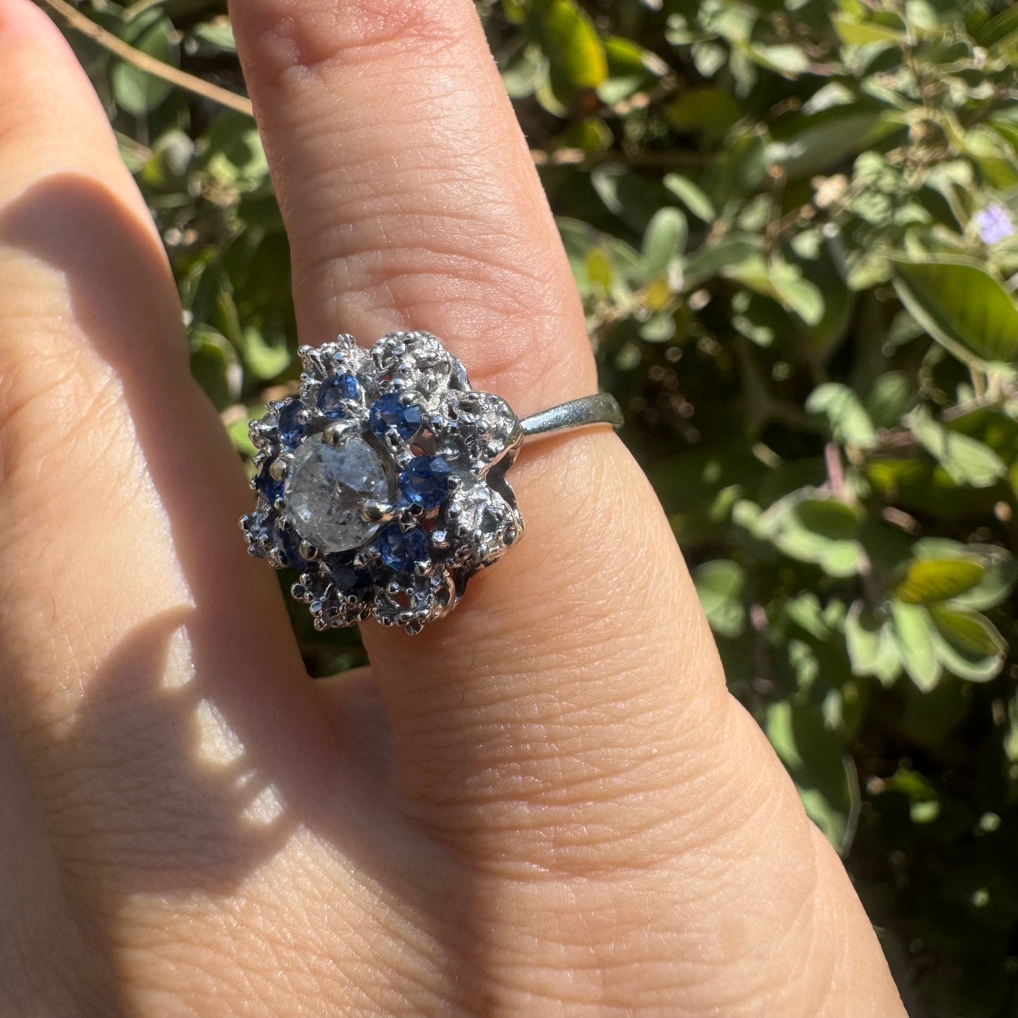 18K gold ring featuring a large round Diamond at the center, surrounded by a floral halo of purple -blue Tanzanite and & Diamonds.