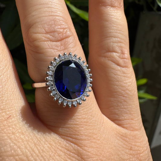 14K gold ring set with a deep blue oval Sapphire surrounded by a halo of sparkling Diamonds