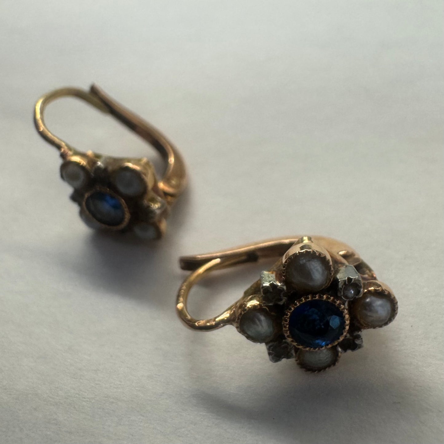 עגילי זהב 14 קראט משובצים אבן ספיר במרכז וסביבה משובצות פנינים קטנות בעיצוב פרחוני