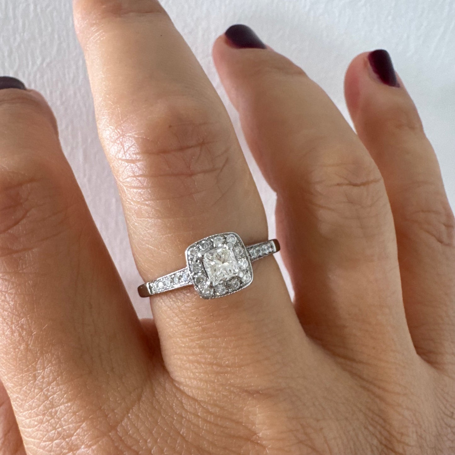 טבעת זהב לבן 14 קראט משובצת יהלום מרכזי בחיתוך פרינסס, מוקף הילת יהלומים קטנים וזרוע משובצת פאווה