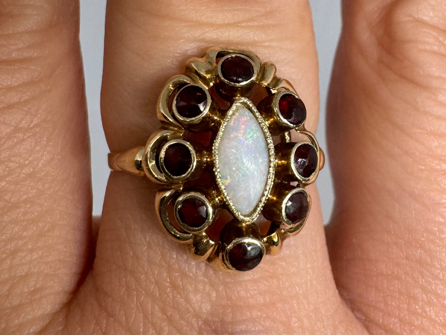 14K gold ring set with a luminous marquise-cut Opal at the center, surrounded by deep red Garnet cabochons
