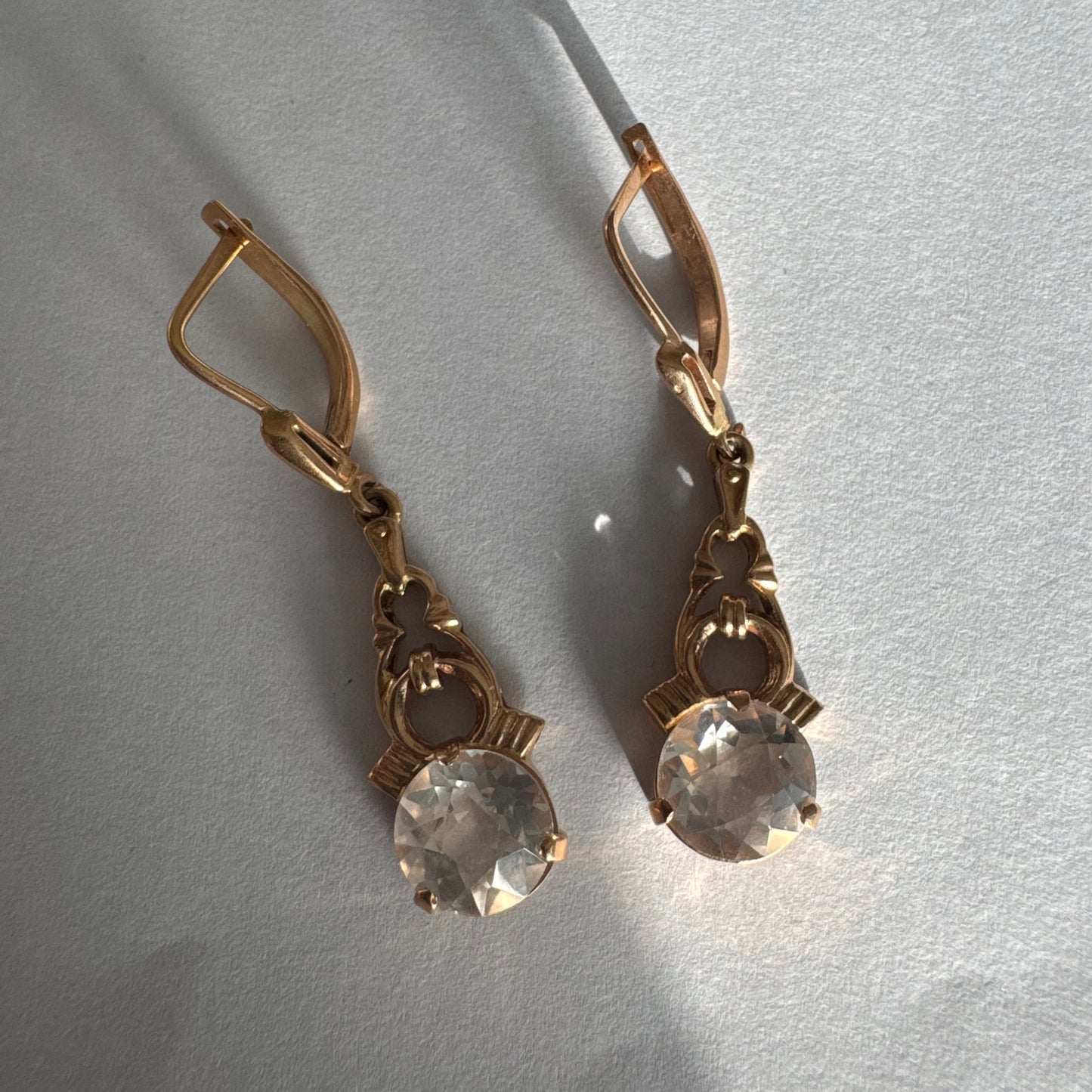 עגילי זהב 14 קראט, תלויים, בעיצוב עדין ונוסטלגי, משובצים באבני חן חתוכות שקופות בסגנון עתיק.