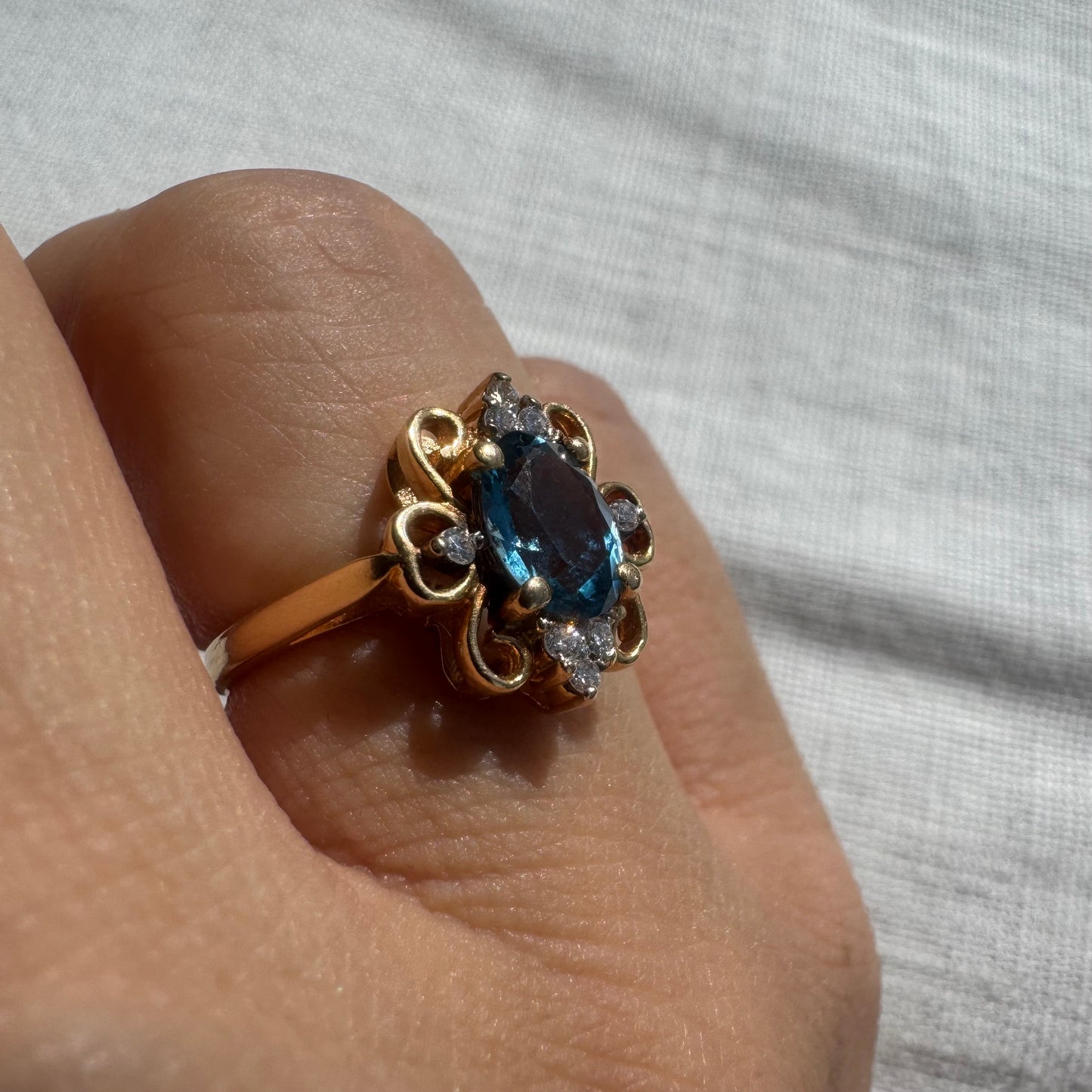 18K gold ring featuring an oval-cut Blue Topaz at the center, accented by sparkling side Diamonds and elegant scroll details.