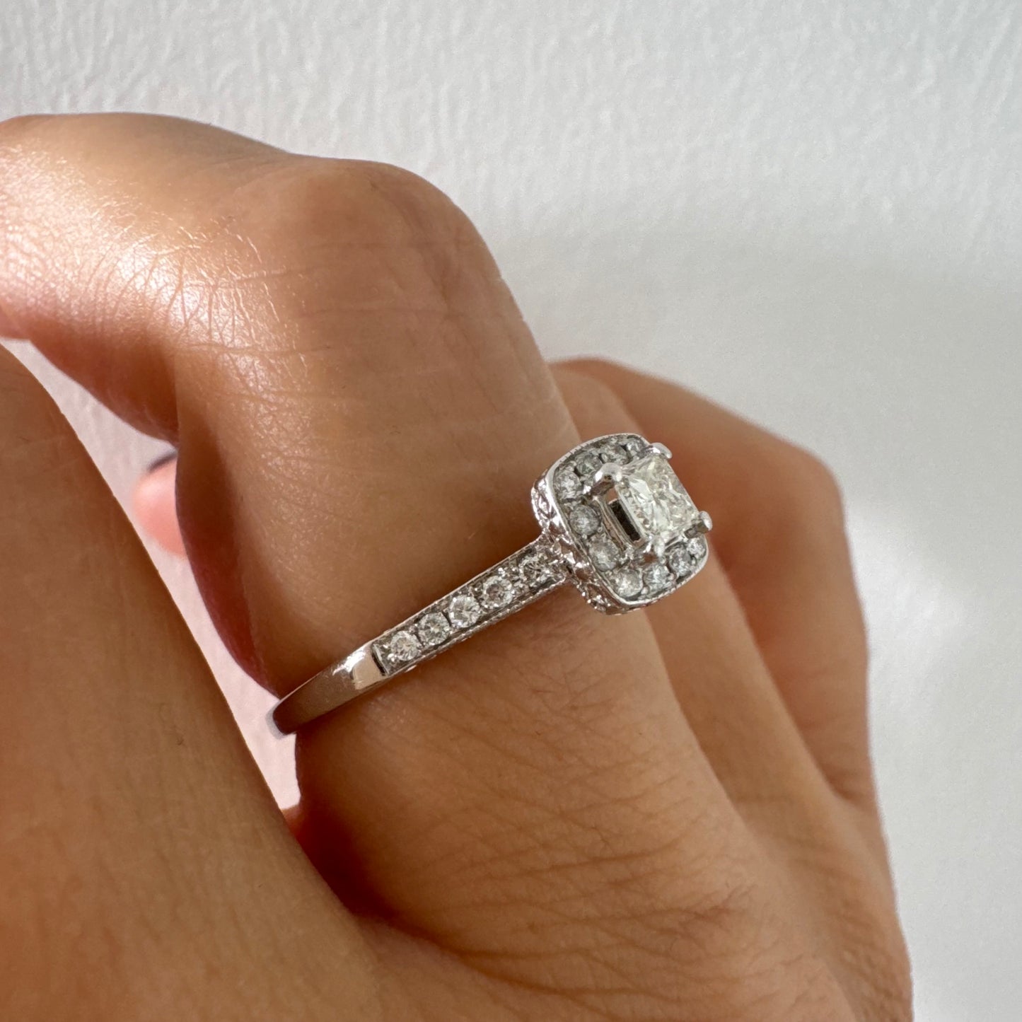 טבעת זהב לבן 14 קראט משובצת יהלום מרכזי בחיתוך פרינסס, מוקף הילת יהלומים קטנים וזרוע משובצת פאווה