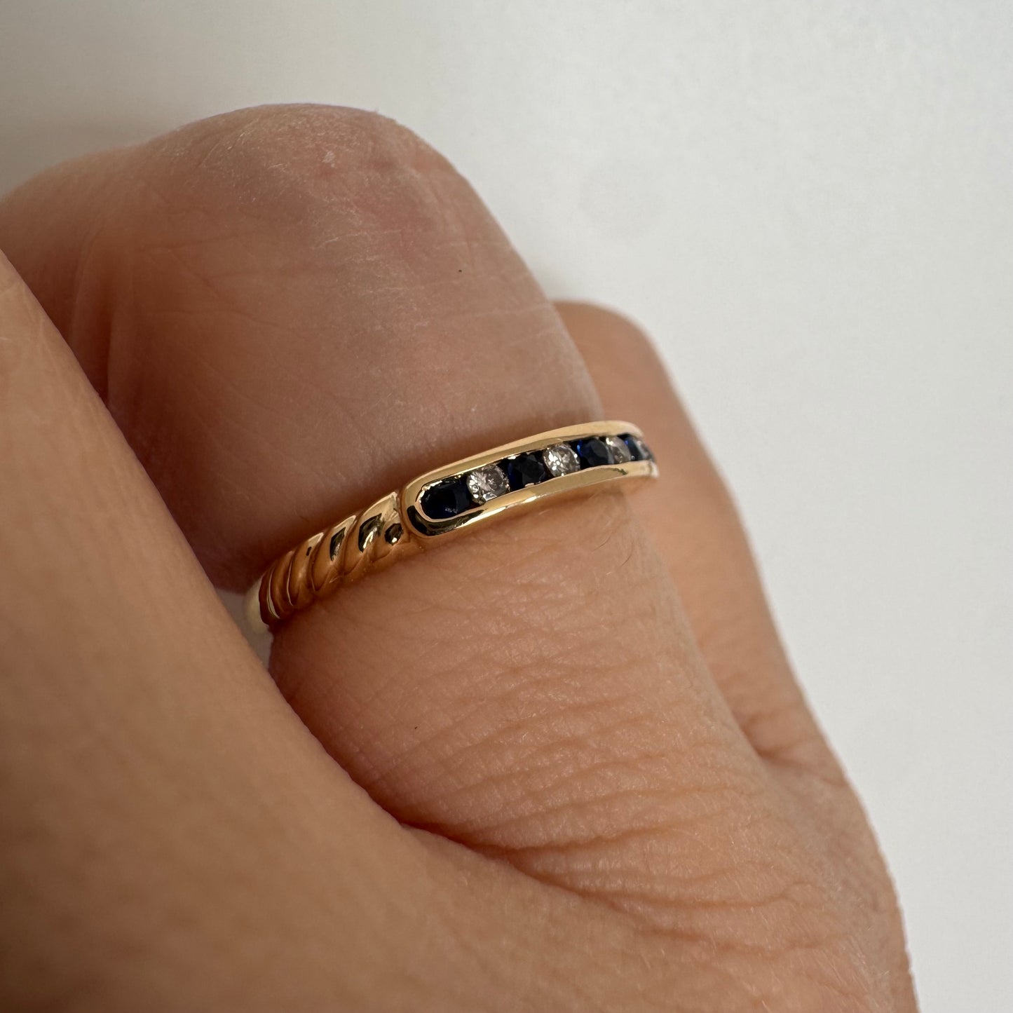 טבעת זהב צהוב 18 קראט בעיצוב נקי ומדויק, משובצת בשורה עדינה של אבני ספיר כחולות וביניהן יהלומים לבנים.