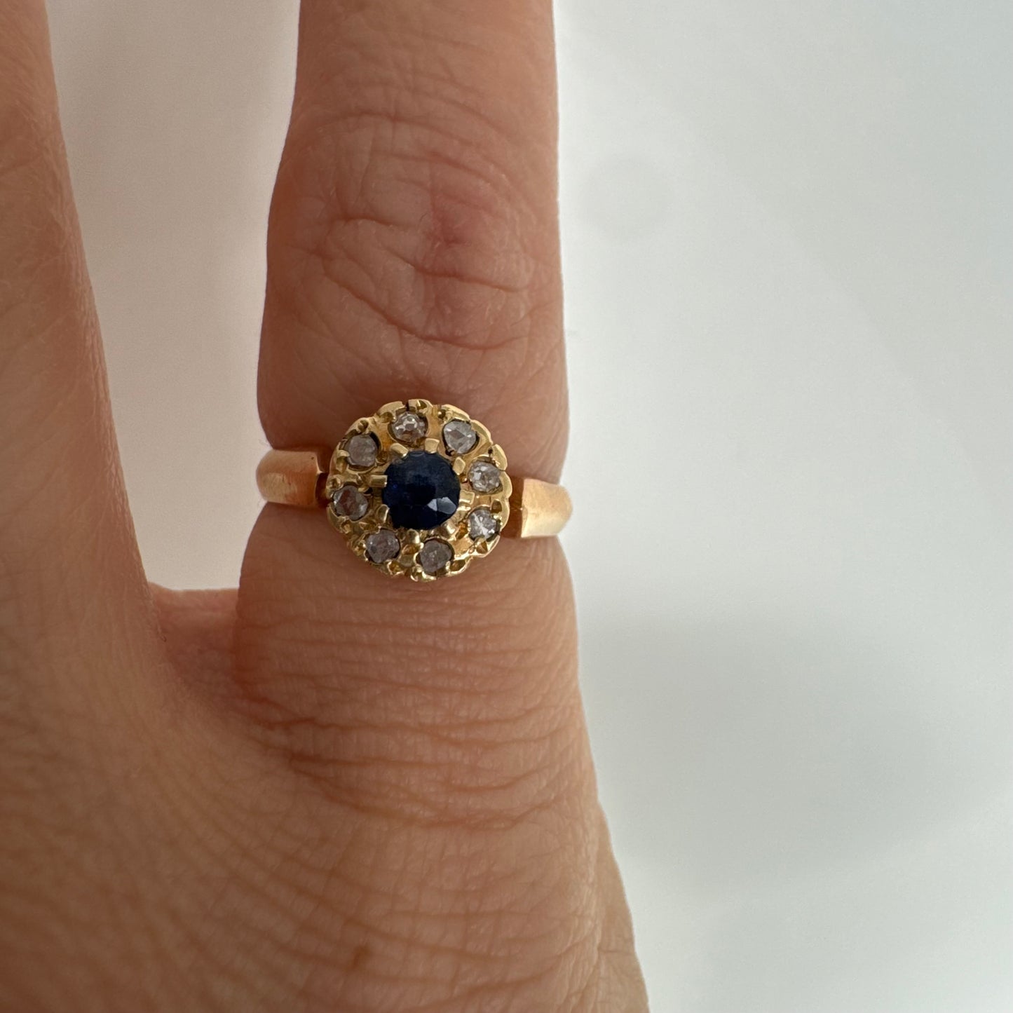 טבעת זהב 14 קראט משובצת ספיר מרכזי מוקף הילה של יהלומים בחיתוך עגול.