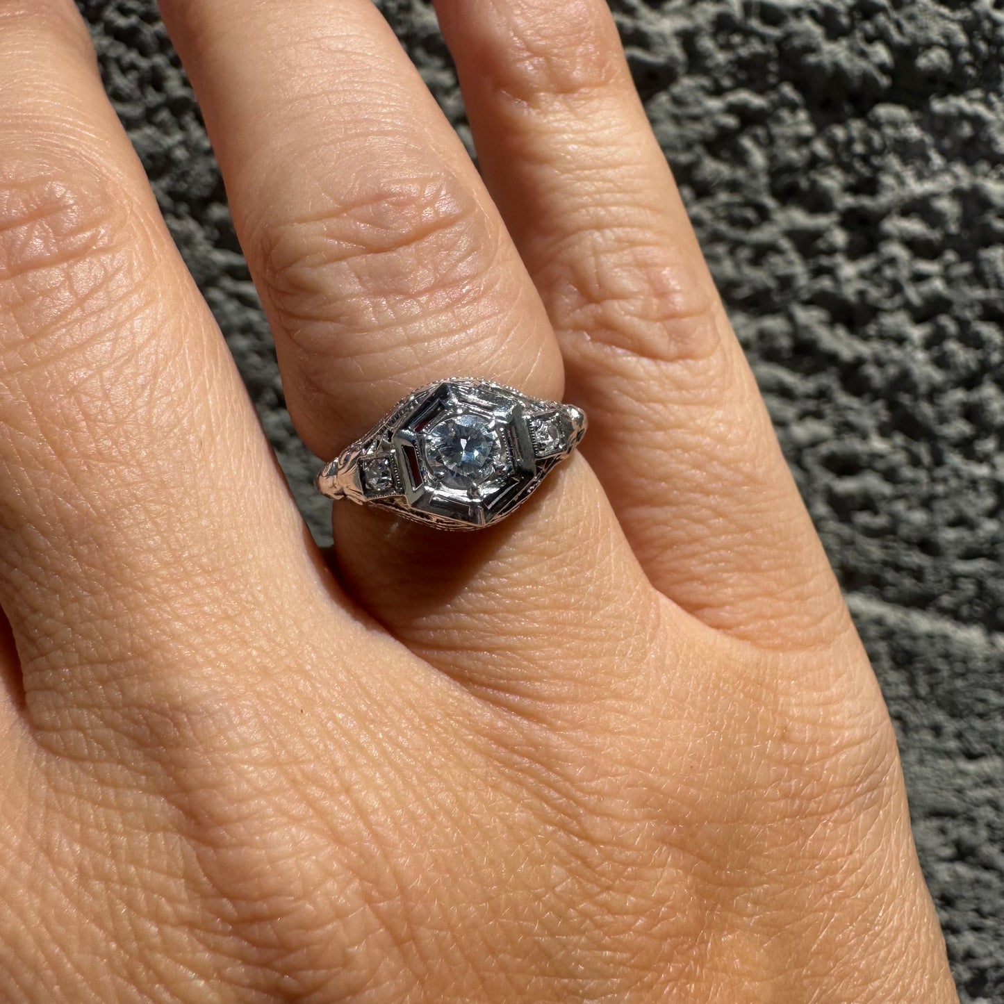 14K gold ring set with a central round diamond, framed by geometric Art Deco details and additional accent stones.