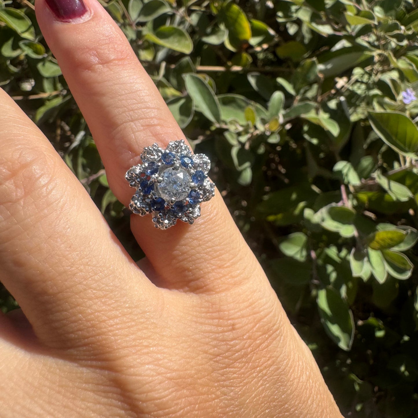 18K gold ring featuring a large round Diamond at the center, surrounded by a floral halo of purple -blue Tanzanite and & Diamonds.