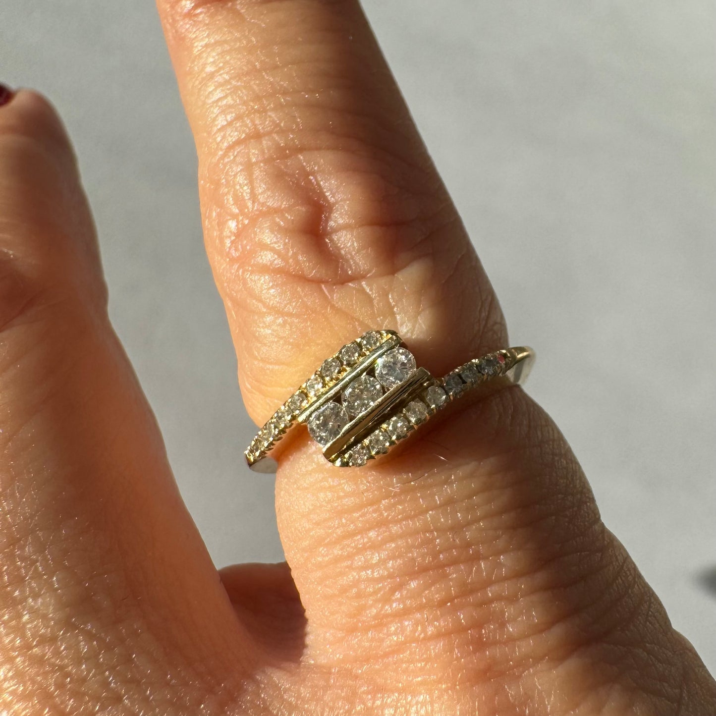 טבעת זהב צהוב 14 קראט בעיצוב ייחודי, משובצת שלושה יהלומים מרכזיים ושורות נוספות של יהלומים לאורך הזרועות. 