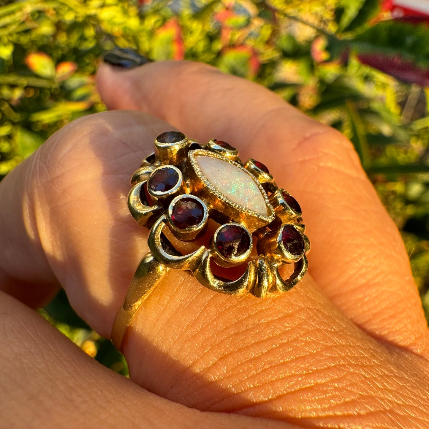 14K gold ring set with a luminous marquise-cut Opal at the center, surrounded by deep red Garnet cabochons