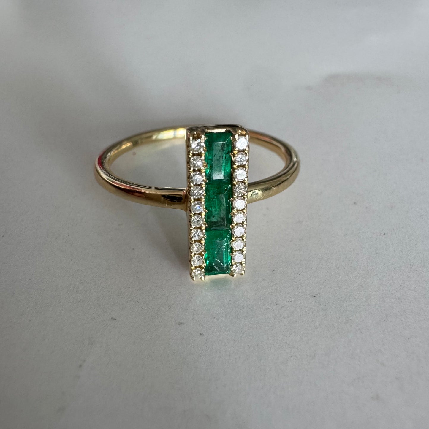 טבעת זהב 14 קראט משובצת אבני אמרלד בחיתוך באגט, מוקפות בשתי שורות של יהלומים נוצצים .