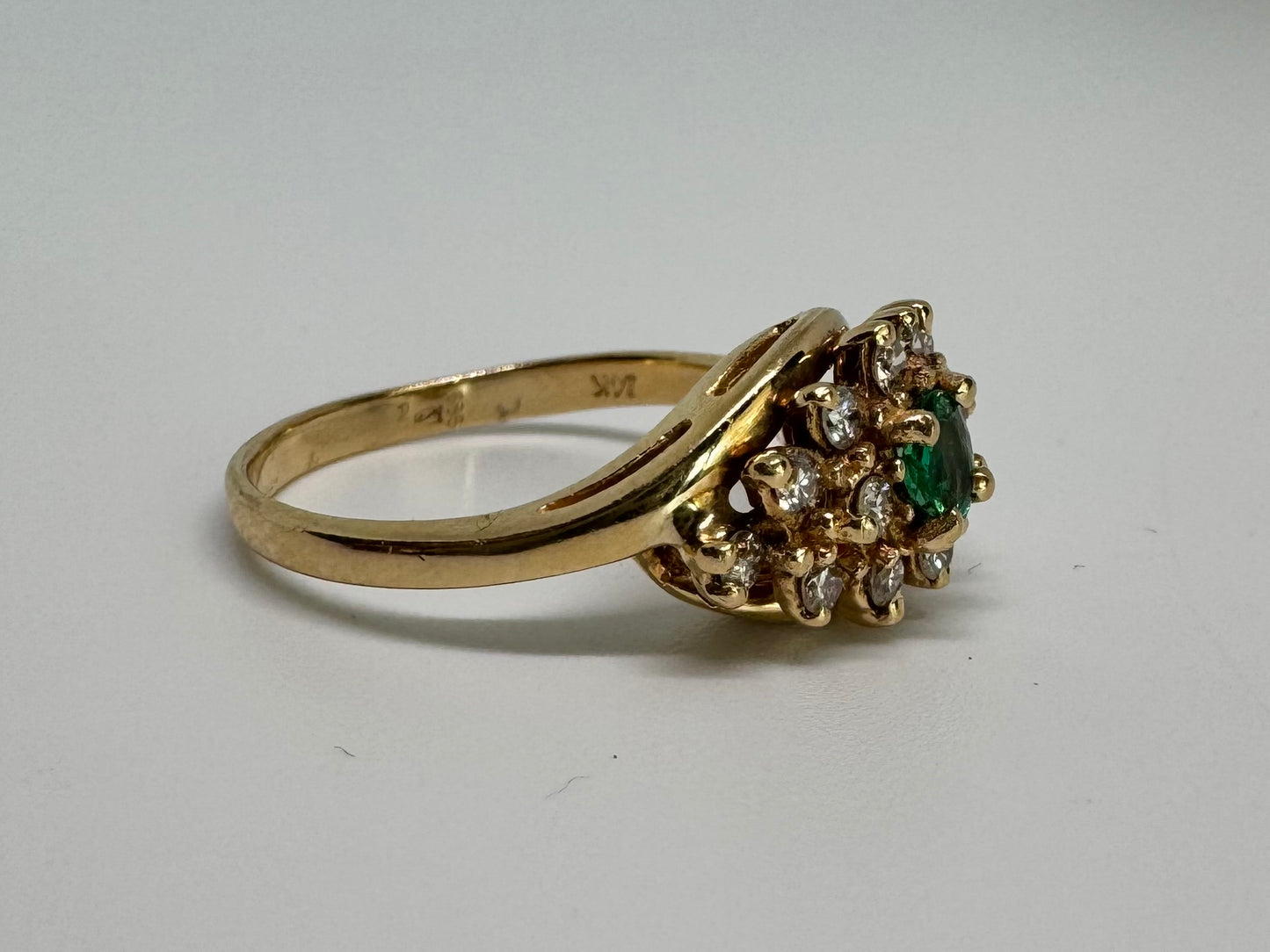 14K gold ring set with Emerald at its center, surrounded by a halo of brilliant-cut diamonds arranged in a floral-inspired cluster