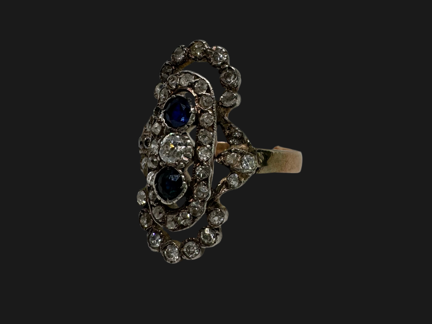 14K gold Antique featuring a stunning trio of gemstones - two deep blue Sapphires surrounding a brilliant old-cut Diamonds